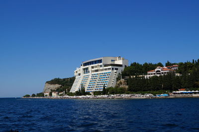 Buildings by sea against clear blue sky