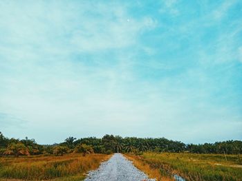 Dirt road amidst field against sky