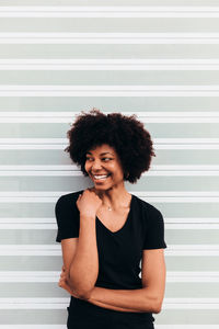 Afro woman laughing against a white wall. she is looking away.