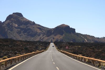 Empty road leading towards mountains against clear sky