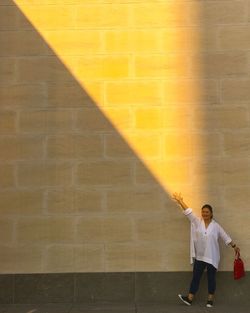 Full length of mature woman with hand raised standing against wall