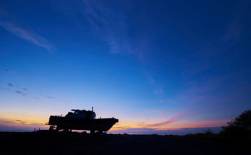 Silhouette boat on land against sky during sunset