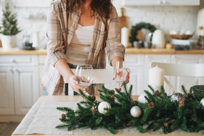 Young woman in the plaid shirt sets festive table with fir composition, christmas time