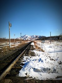 Railroad tracks on snowcapped field against sky