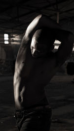 Shirtless man stretching arms in darkroom