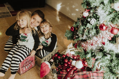 Brother embracing sisters by christmas tree at home