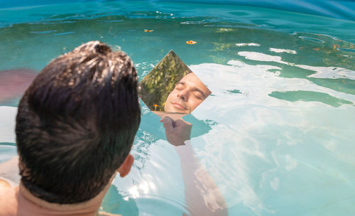 Reflection of man in mirror while sitting in swimming pool