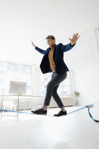 Smiling businessman with arms outstretched balancing on tightrope in office