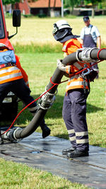 Firefighters holding pipe on road amidst grass field