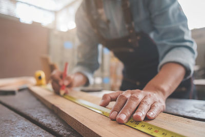 Midsection of carpenter measuring plank in workshop