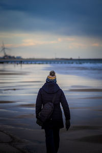 Rear view of woman standing at beach during sunset