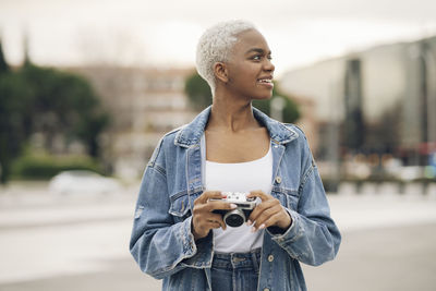 Young woman looking away holding old camera