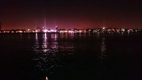 Illuminated cityscape by river against sky at night