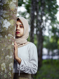 Portrait of teenage girl standing against tree trunk