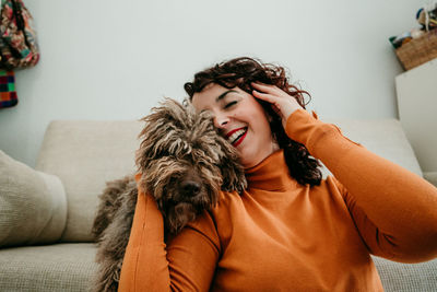 Happy woman holding dog sitting on sofa at home