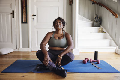 Mature woman with eyes closed practicing relaxation exercise on mat at home