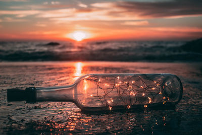 Close-up of string light in bottle at beach against sky during sunset