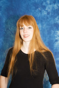 Portrait of beautiful smiling woman with redhead standing against blue background