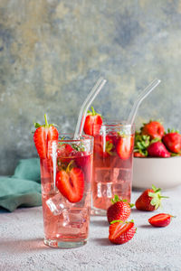 Refreshing cocktail with strawberries in glasses with a straw on the table and a bowl with berries.