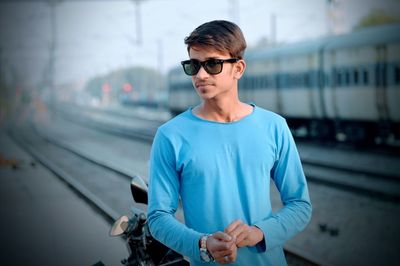 Young man wearing sunglasses with train in background