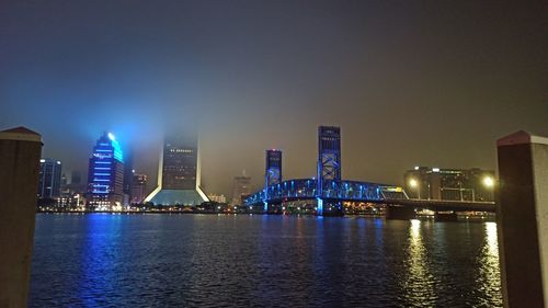 Illuminated city by river against sky at night