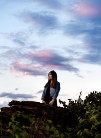 Low angle view of thoughtful young woman standing on mountain against sky during sunset