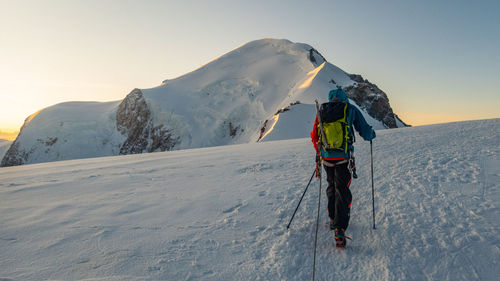 Rear view of man walking on snow covered mountain during sunset