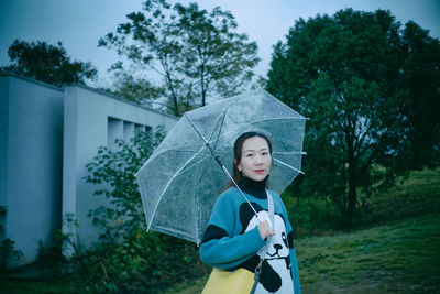 Portrait of woman with umbrella standing against trees