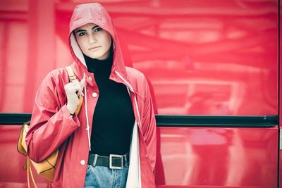 Portrait of beautiful young woman standing against red wall