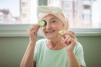 Mature woman covers eyes with cucumber and enjoys life at home, wellness and beauty care at any age