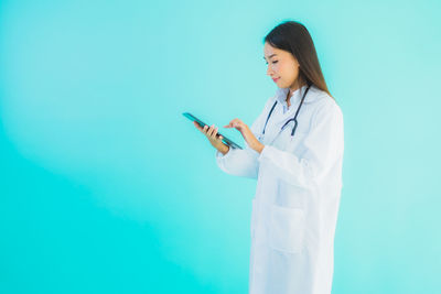 Young woman using phone while standing against blue background