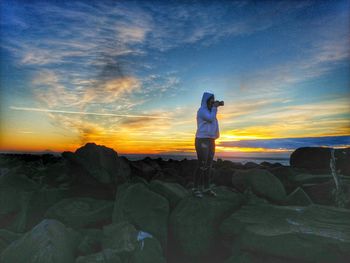 Woman standing on rocks by sea against sky during sunset