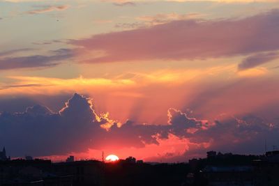 Silhouette cityscape against dramatic sky during sunset