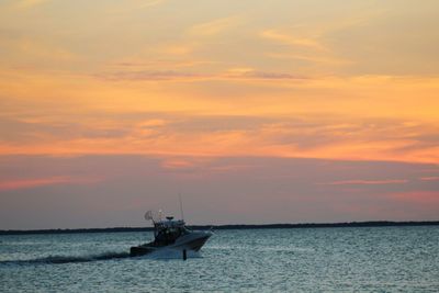 Motorboat sailing on sea against sky during sunset