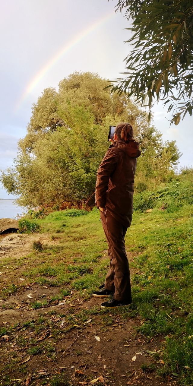 MAN PHOTOGRAPHING ON FIELD AGAINST TREES