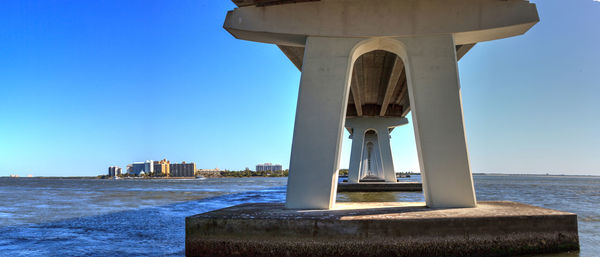 Bridge over sea by buildings against clear blue sky