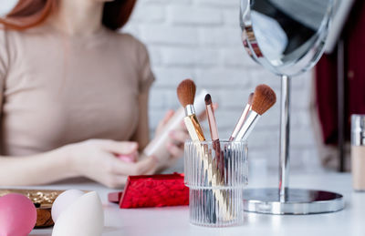 Young beautiful woman holding make-up brushes and making up with cosmetics set at home