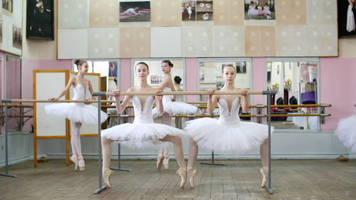 In the ballet hall, girls in white ballet tutus, packs are engaged at ballet, rehearse plie forward