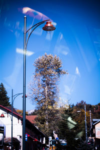 Illuminated street light by trees against sky