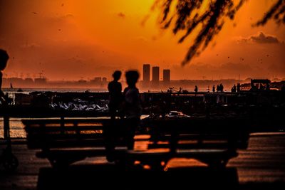 Silhouette people standing by sea against sky during sunset