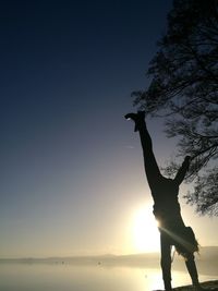 Woman doing handstand on cliff by lake at sunrise