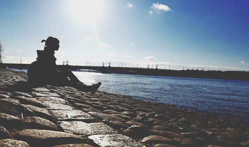 Man sitting on rock by sea against sky
