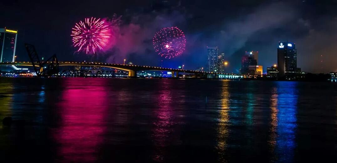 illuminated, night, water, architecture, built structure, waterfront, reflection, long exposure, river, city, sky, building exterior, connection, arts culture and entertainment, bridge - man made structure, firework display, glowing, travel destinations, multi colored, motion