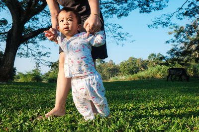 Low section of mother with cute son standing on grassy land in park