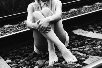Low section of woman sitting on railroad track