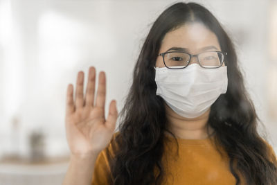 Portrait of beautiful young woman wearing mask looking through glass window