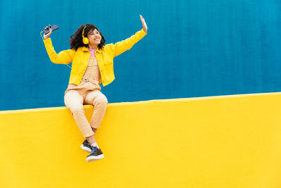 Low angle view of woman sitting on yellow wall