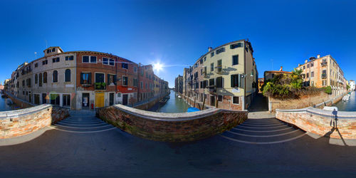 Fish-eye view of canal amidst buildings in city against clear sky