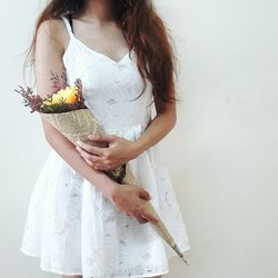 Midsection of woman holding bouquet while standing against wall