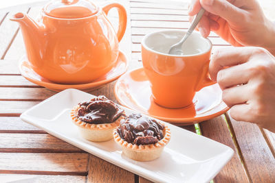 Cropped hand of woman stirring tea in cup by tart and teapot served on table